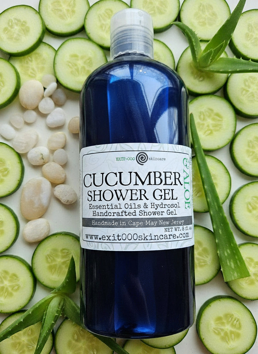 A bottle of Cucumber Aloe Shower Gel with a label that includes the product name and a brief description. The bottle is dark blue with a light blue label and is presented with a background of decorative stones.