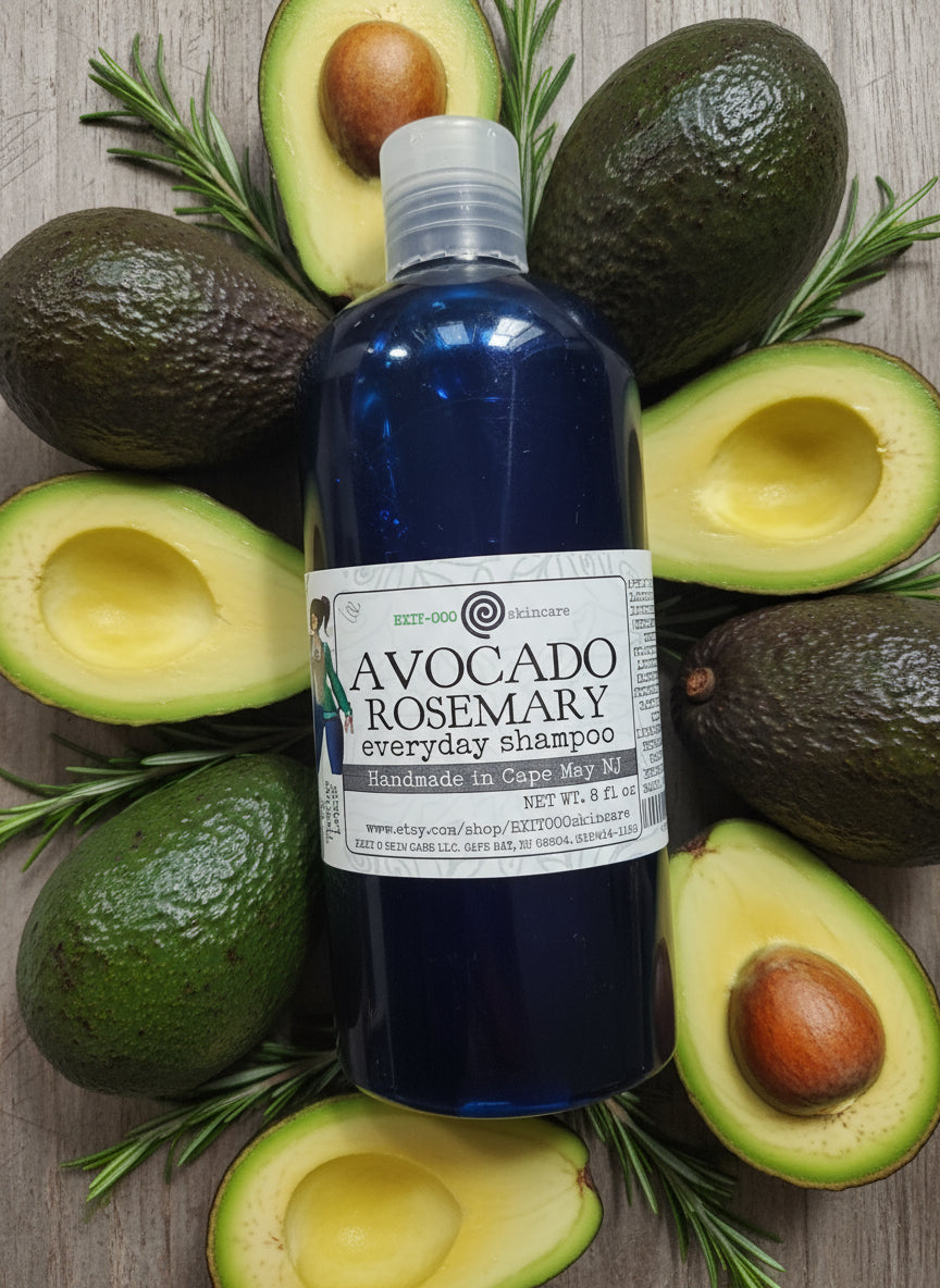 Bottle of Avocado Rosemary shampoo surrounded by avocados and rosemary on a wooden surface