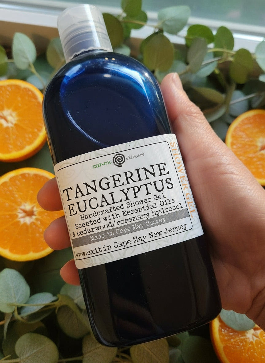 A bottle of Tangerine Eucalyptus Shower Gel with a label that includes the product name and a brief description. The bottle is held in hand.