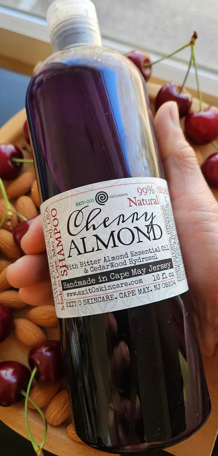 A hand holding a bottle of Cherry Almond Oatmeal shampoo with a label that provides product information.