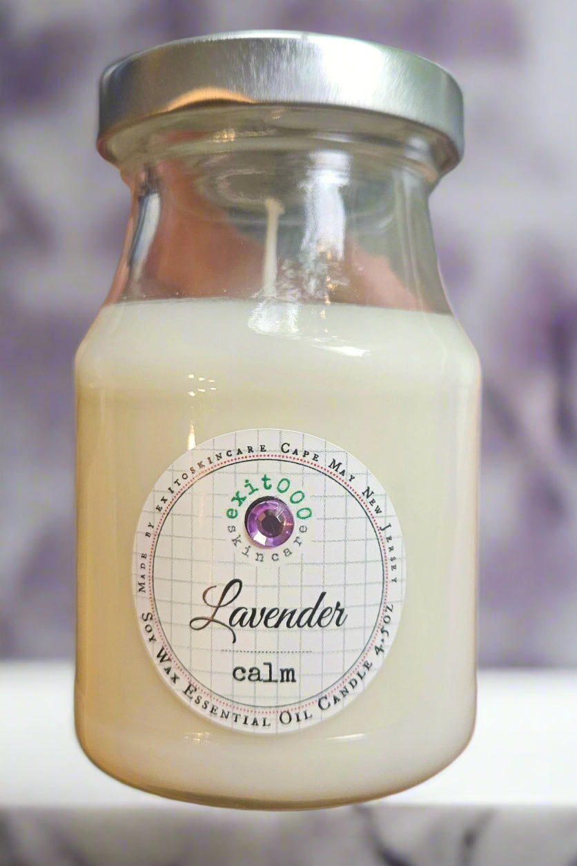 Glass candle jar labeled 'Lavender Calm' with a blurred purple background