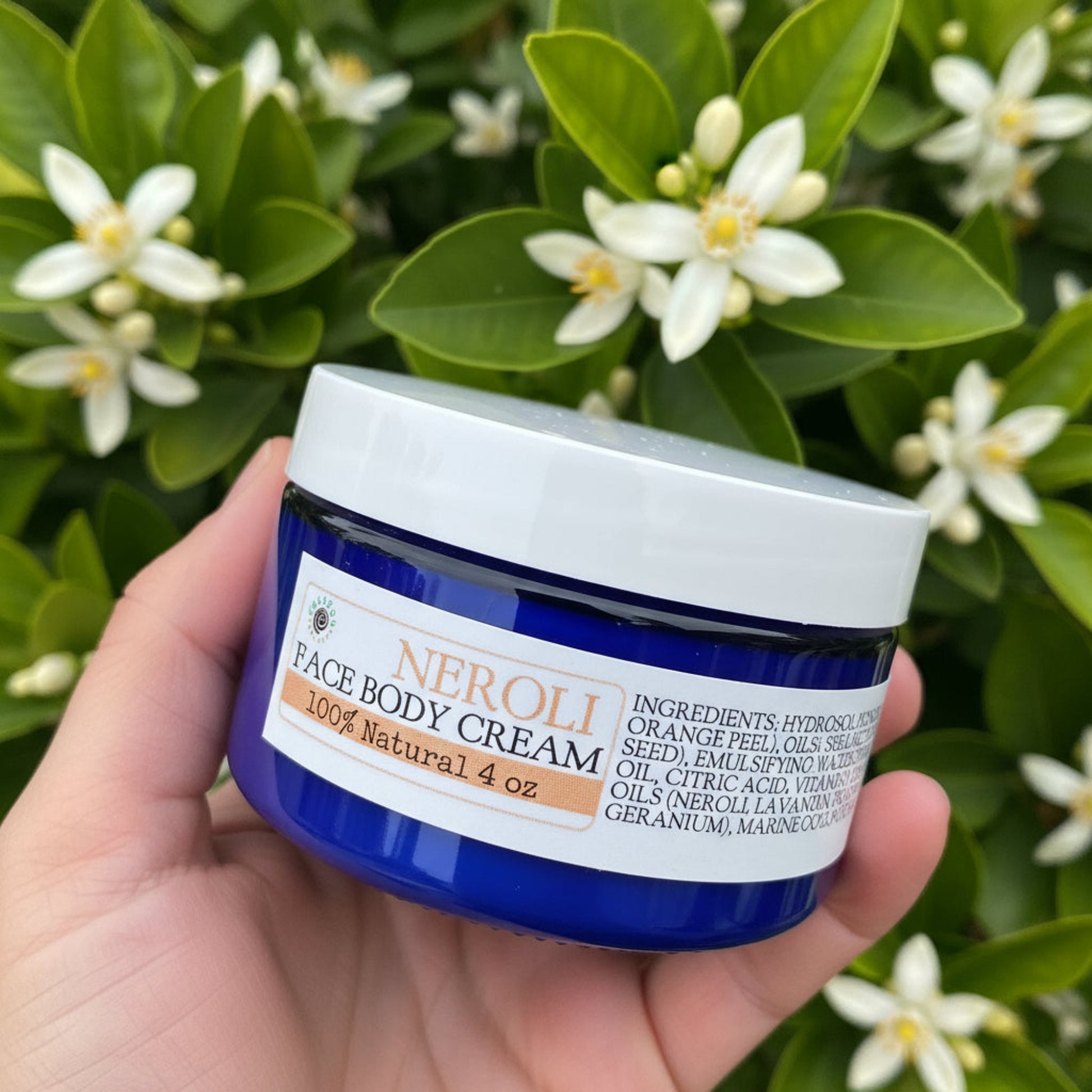Jar of Neroli Face Body Cream held in a hand with a blurred background