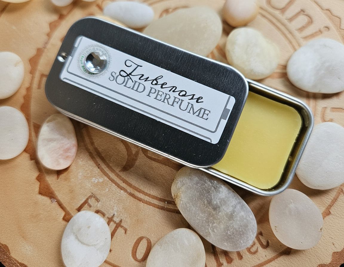 Solid perfume bar in a tin surrounded by stones on a textured surface