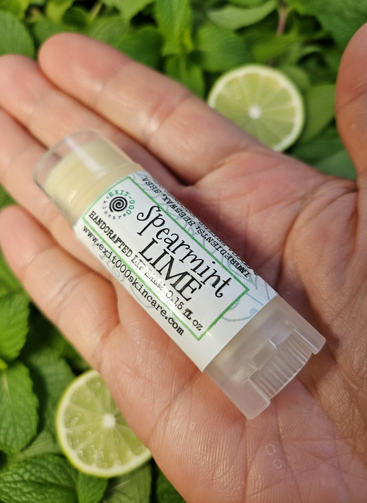 Lip balm stick labeled 'Spearmint Lime' held in a hand against a wooden surface.