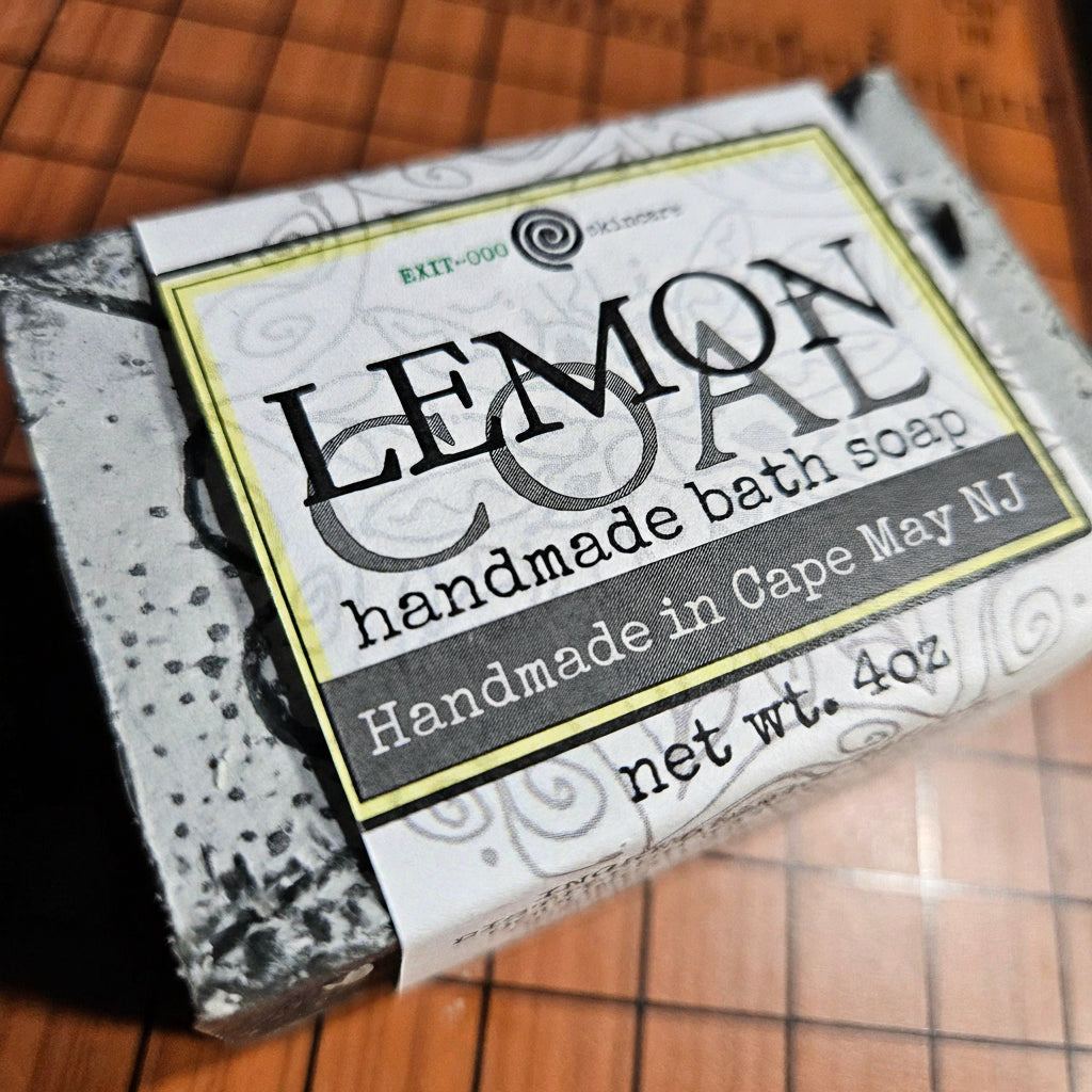 A bar of soap with a label that reads 'LEMON COAL BATH SOAP, HANDMADE DELICA', indicating it is an 4 oz (125g) bar of soap with activated charcoal, and it is made with 100% olive oil.