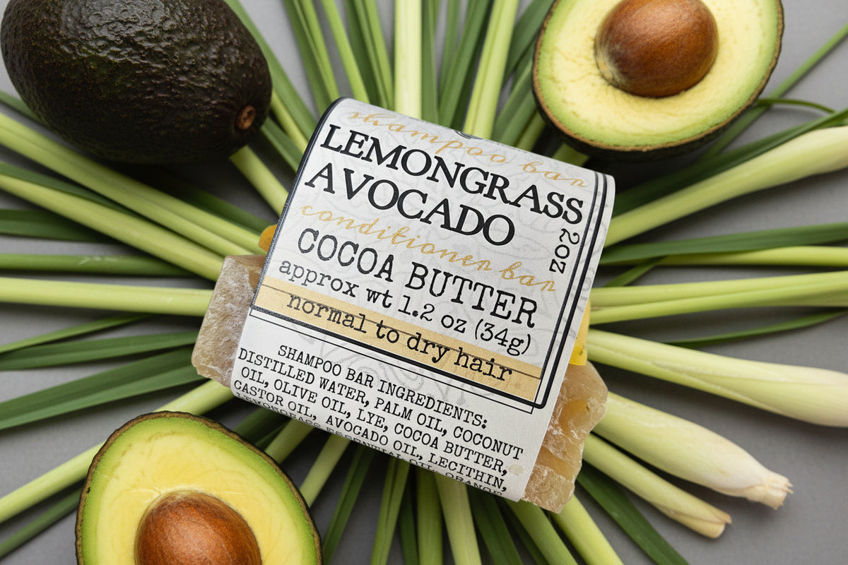 A packaged shampoo bar labeled Lemongrass Avocado Conditioner Bar in Cocoa Butter, shown wrapped in a paper label with visible tan bar soap at the ends on a light textured background.