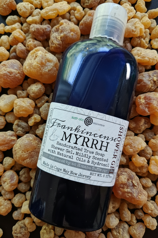 A dark-colored bottle of Frankincense Myrrh Shower Gel with a label displaying the product name and ingredients such as olive oil and shea butter.