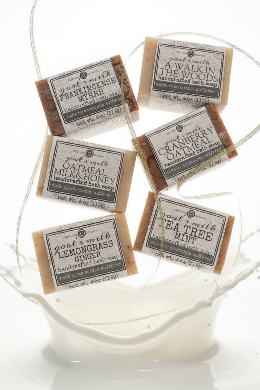 A set of six different goat's milk soap bars with labeled packaging, displayed on a patterned surface.