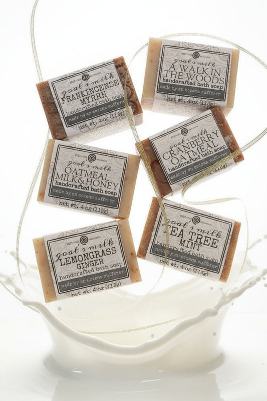 A set of six different goat's milk soap bars with labeled packaging, displayed on a patterned surface.
