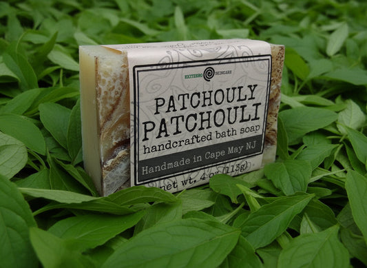 A bar of soap with a beige base and brown edges, featuring a label that reads 'PATCHOULI PATCHOULI handcrafted bath soap made by an essential soaps', indicating it is a Patchouli-scented product.